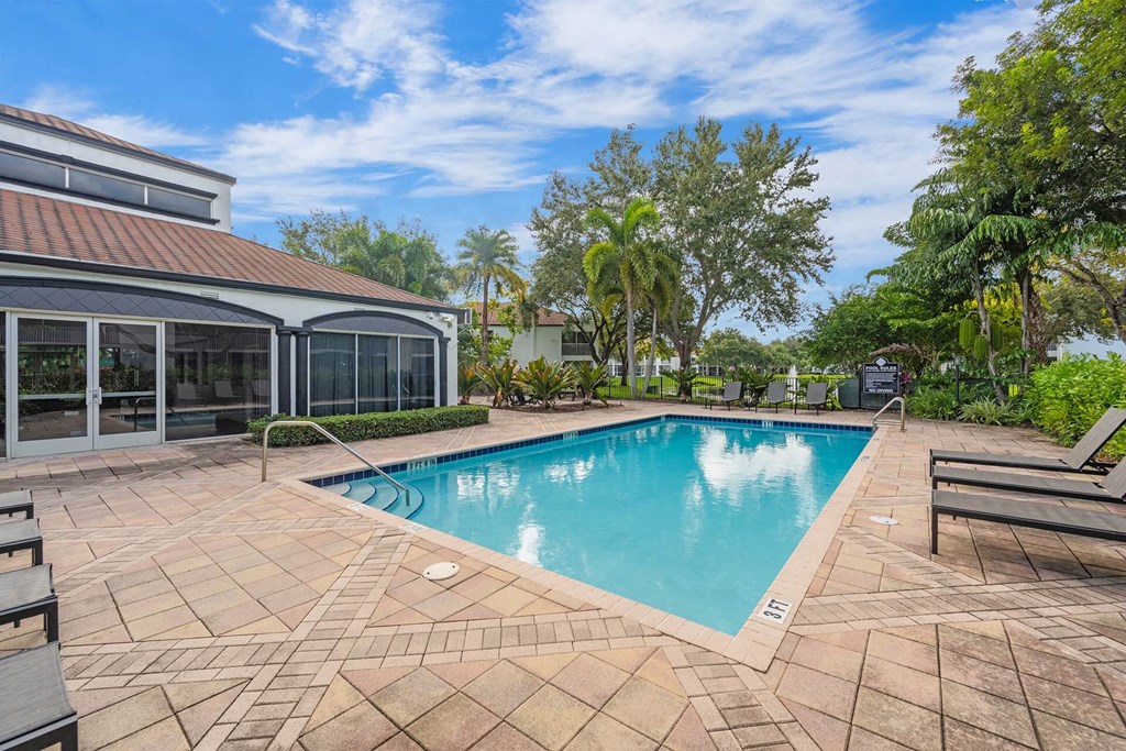 A swimming pool surrounded by a tiled patio and a house with a glass wall.