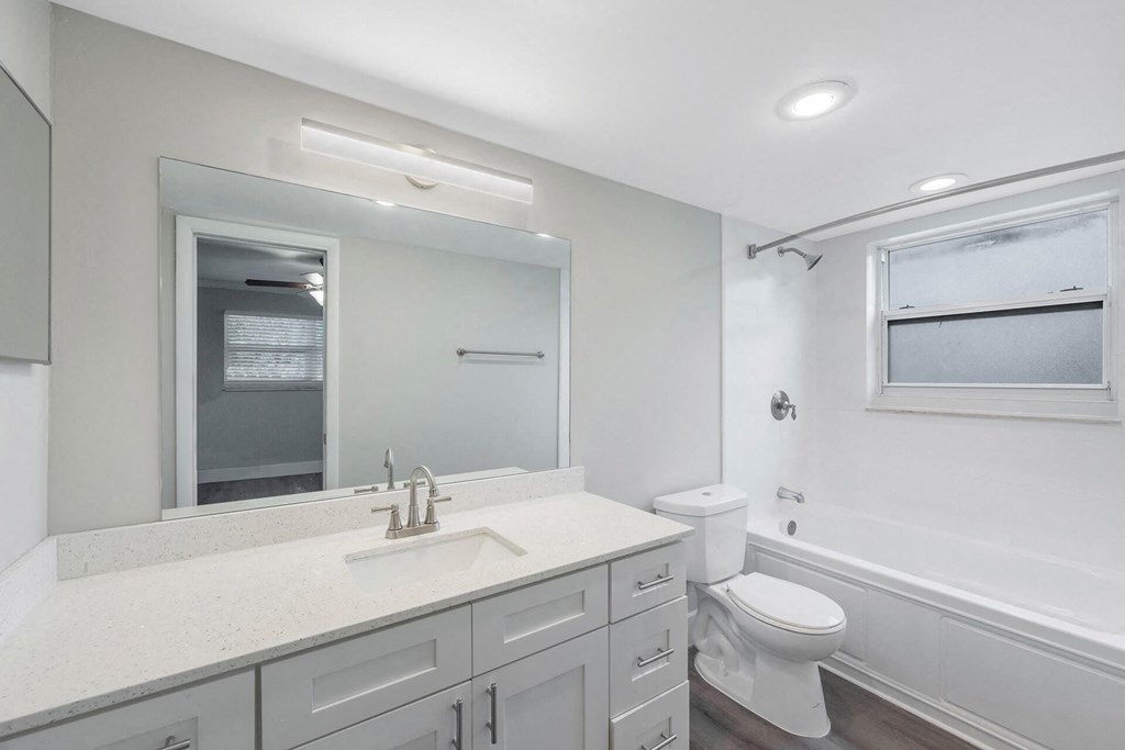 A white bathroom with a sink, mirror, toilet and tub.