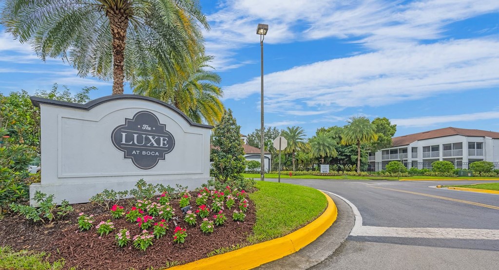 A sign for Luxe at Boca is in front of a palm tree.