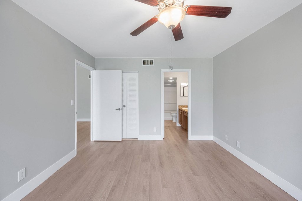A room with a ceiling fan and light fixture, two doors, and a wooden floor.