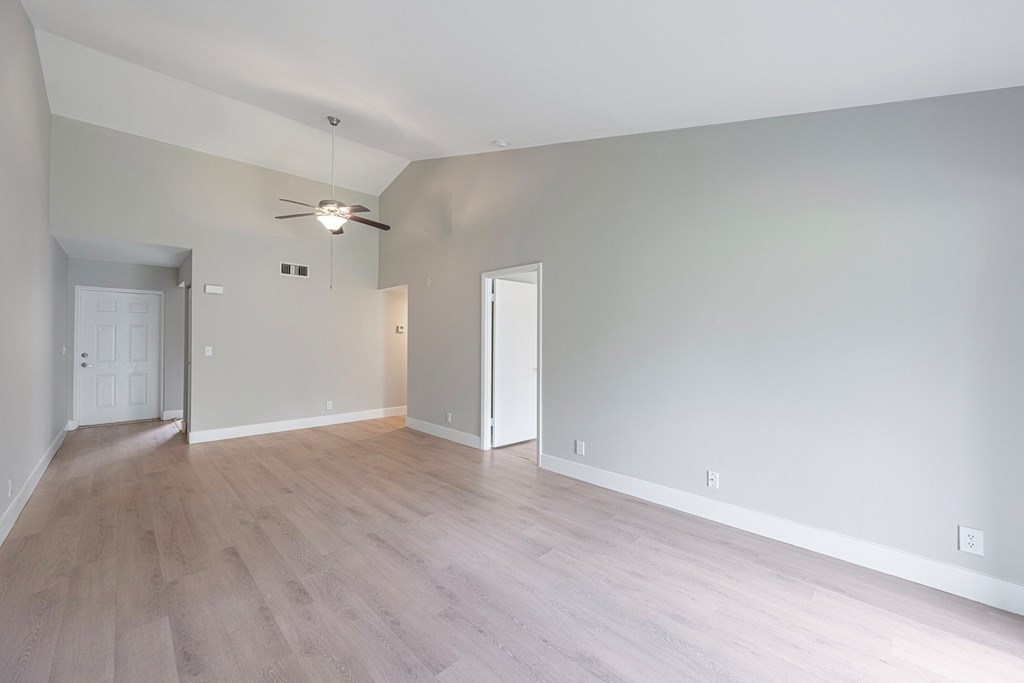 A room with a ceiling fan and light fixture, and a doorway leading to another room.