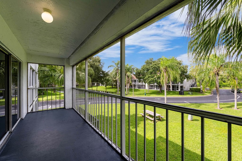 A balcony with a view of a green lawn and trees.