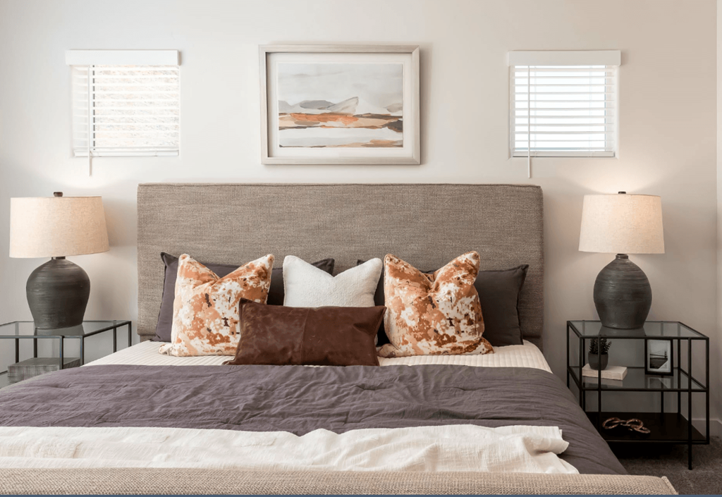 A bed with a grey headboard and a grey comforter with a white pillow and a brown pillow with a white pillow and a picture on the wall.