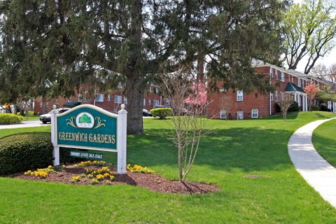 A sign for Greenwich Gardens is in the foreground of a well kept lawn.