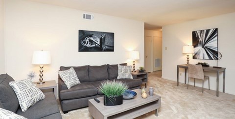 A living room with a grey couch, a black and white picture on the wall, and a wooden coffee table with a plant on it.