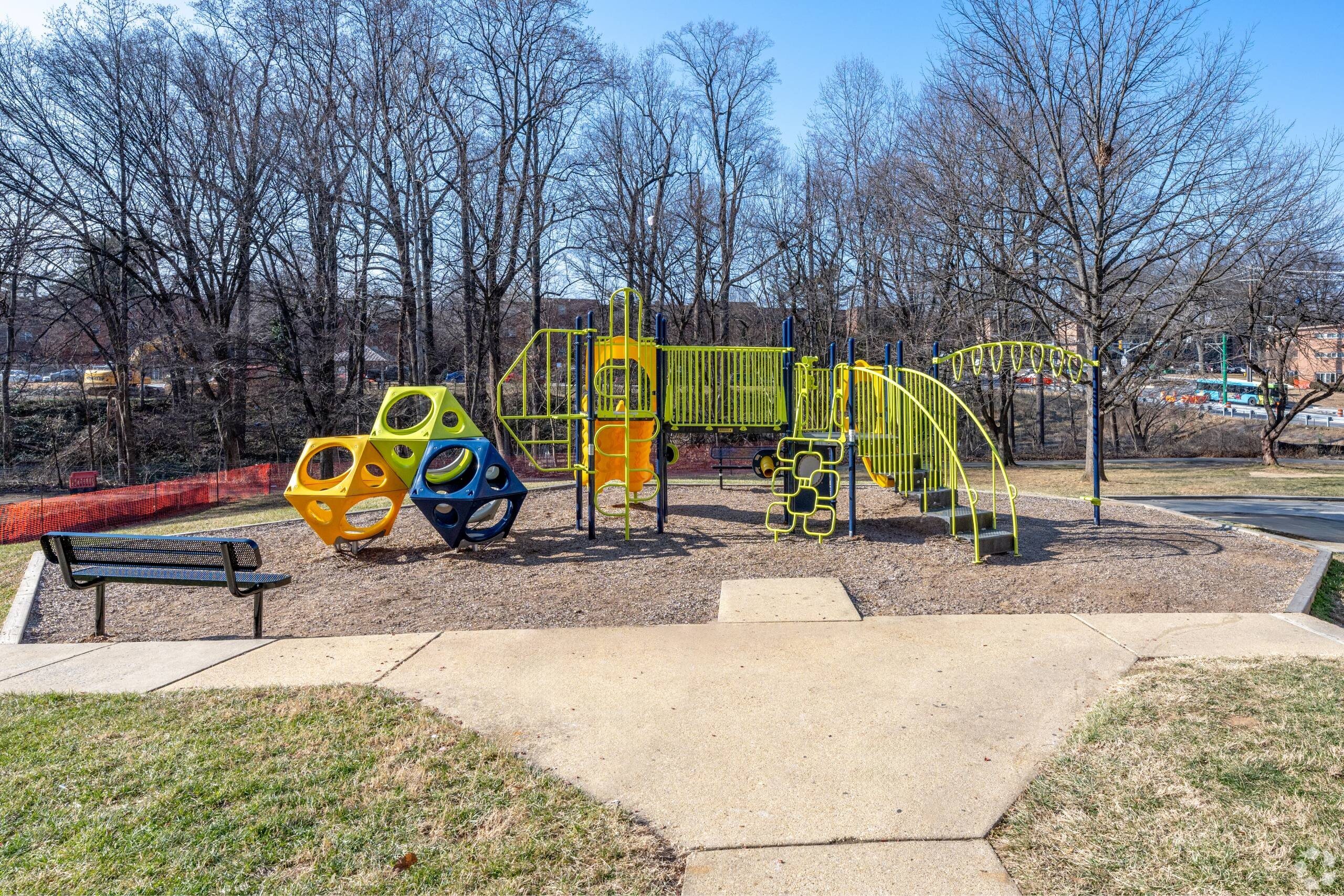 A playground with a yellow slide and a red bench.