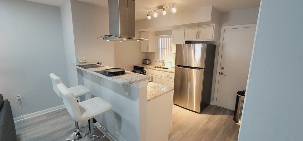 A kitchen with a stainless steel refrigerator and white bar stools.
