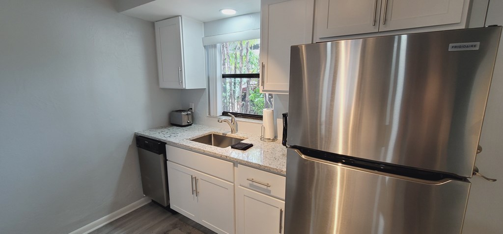 A kitchen with a stainless steel refrigerator and white cabinets.
