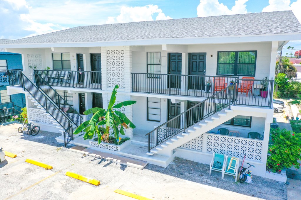 A white building with a balcony and a palm tree in front.