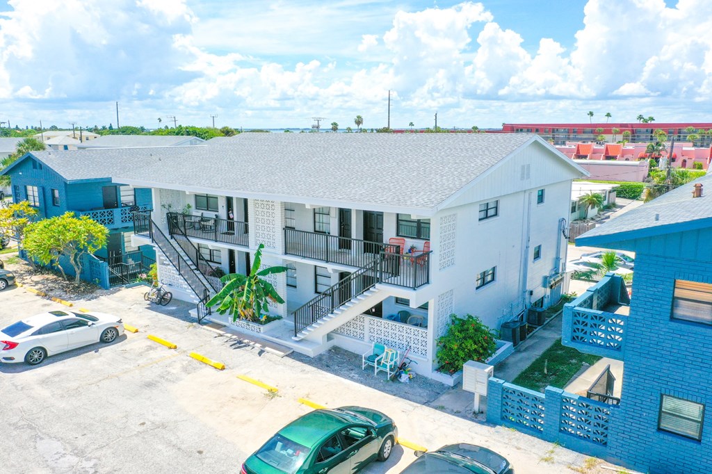 A white building with a blue roof and a green car parked in front.