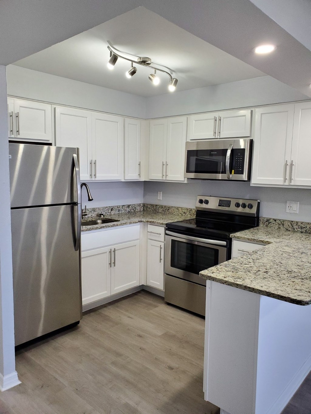 A kitchen with a stainless steel refrigerator, microwave, oven, and wooden flooring.
