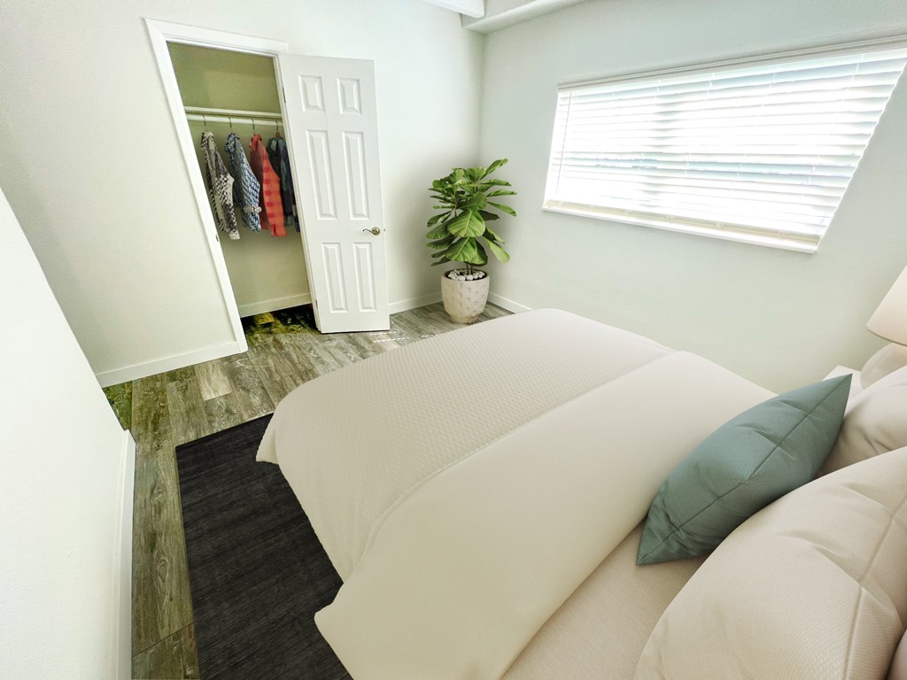 A white couch with a green pillow sits in front of a white door with clothes hanging on it.