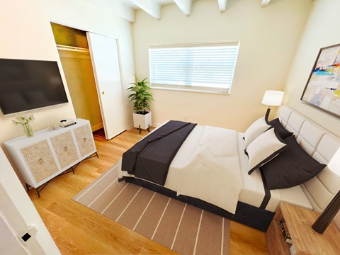 A bedroom with a bed, a television, a plant, and a painting on the wall.