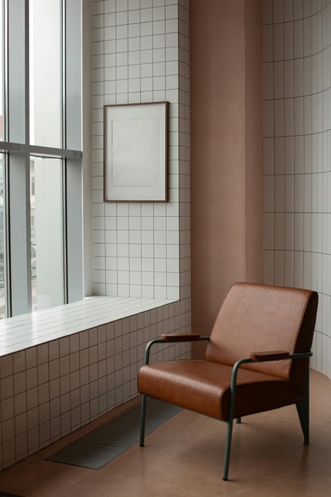 A brown leather chair sits in front of a window with a white frame and a picture on the wall.