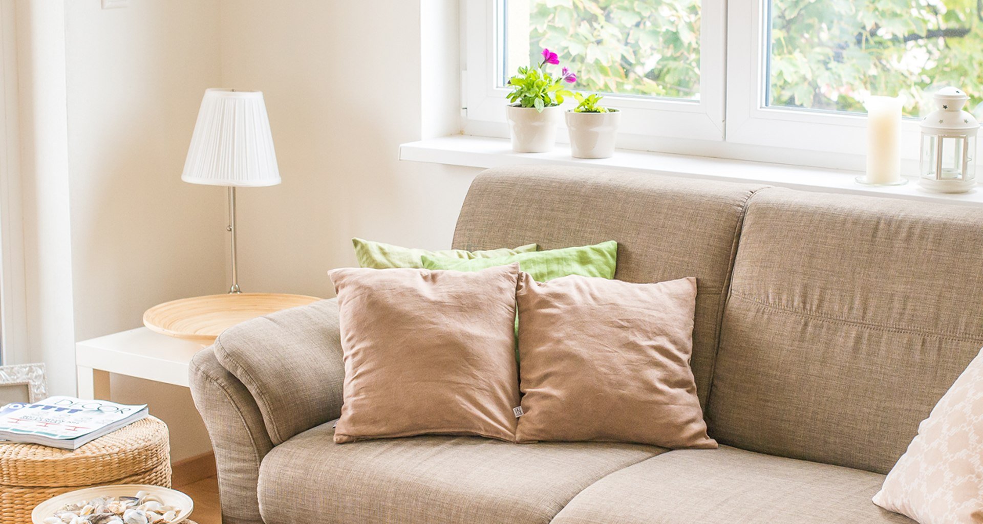 A beige couch with two pillows and a small table with a lamp on it.
