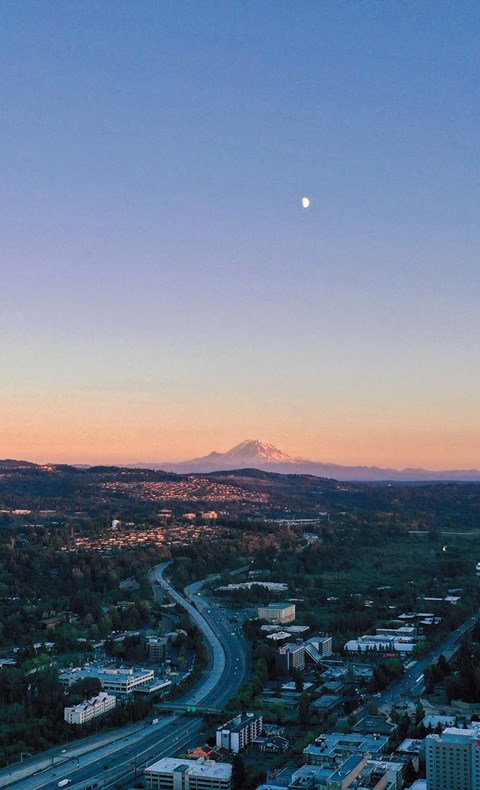 A cityscape with a mountain in the background and a crescent moon in the sky.