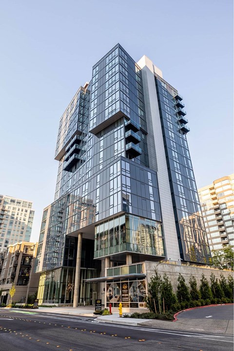A modern glass building with a curved design stands tall among other buildings.