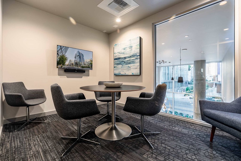 A conference room with a table surrounded by chairs and a television on the wall.