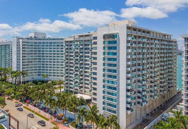 A large white building with many windows is surrounded by palm trees.