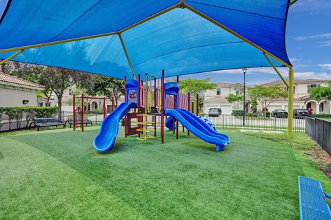 Gate enclosed, covered playground with a blue slide and a green canopy.