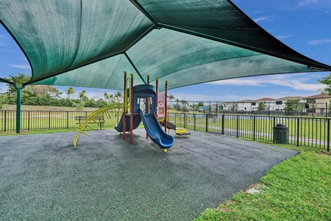 Gate enclosed, covered playground with a blue slide and a green canopy.