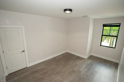 A room with a white door and a window with a view of trees.