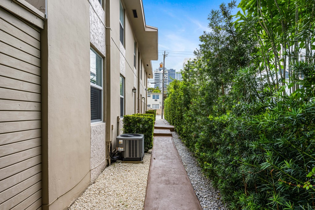 A narrow pathway leads between two buildings with a green hedge on the right.