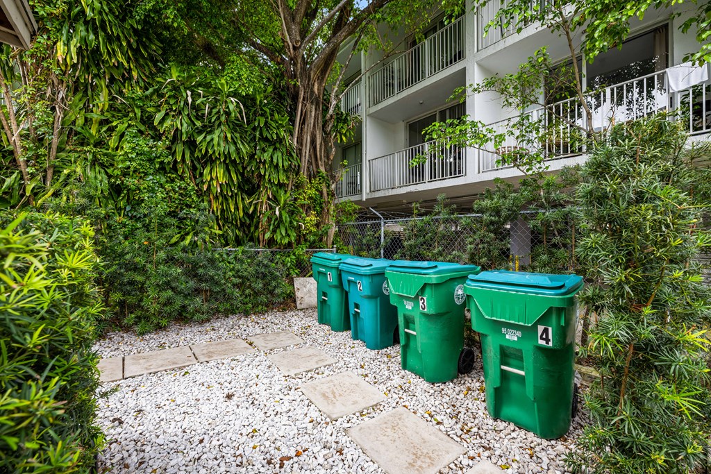 Four green bins are lined up in a garden.