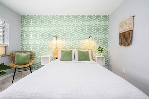 A bedroom with a white bed and green patterned wallpaper.