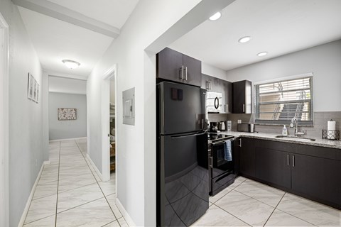 A black refrigerator is in a kitchen with white walls.