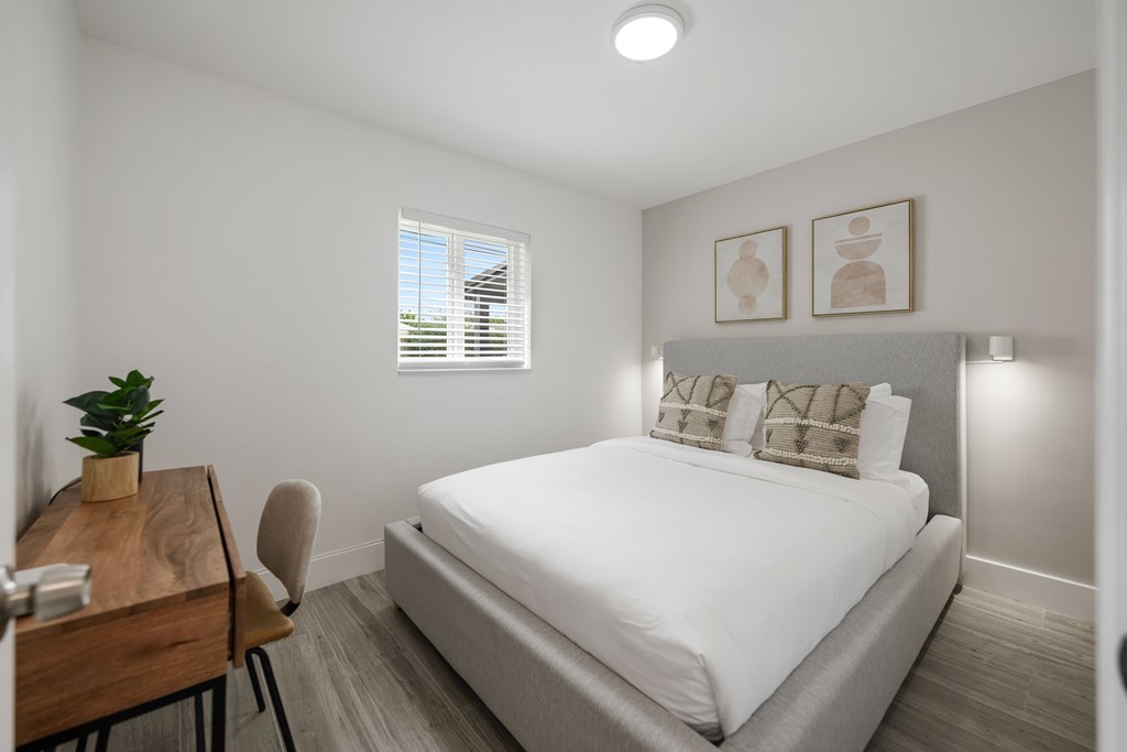 A bedroom with a bed, chair, and a small table with a plant on it.