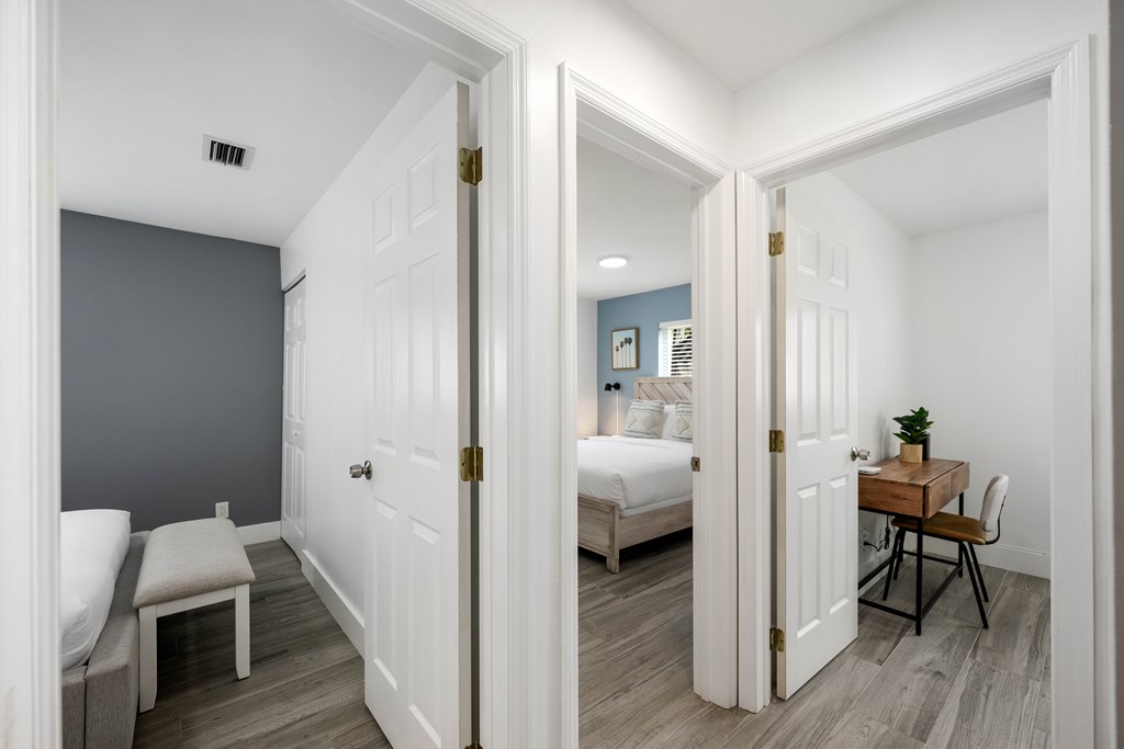 A white door opens to reveal a bedroom with a bed and a desk.