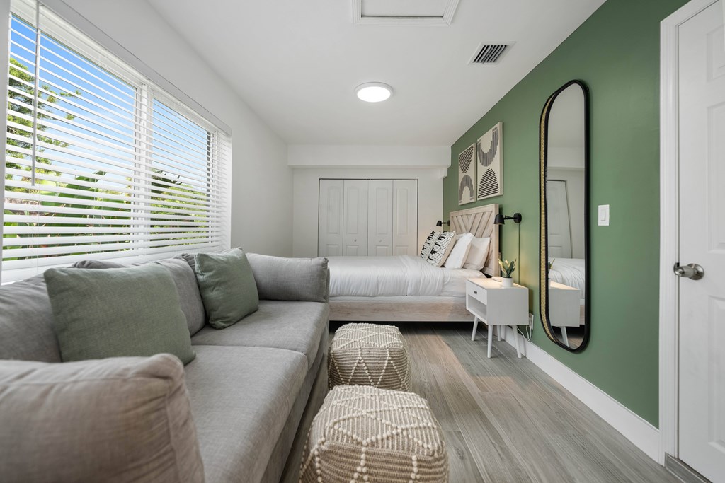 A room with a grey couch and a green wall.