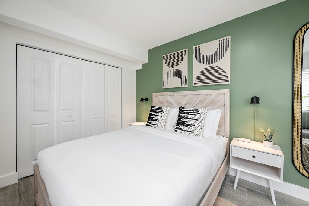 A bedroom with a white bed, a white nightstand, and a green wall.
