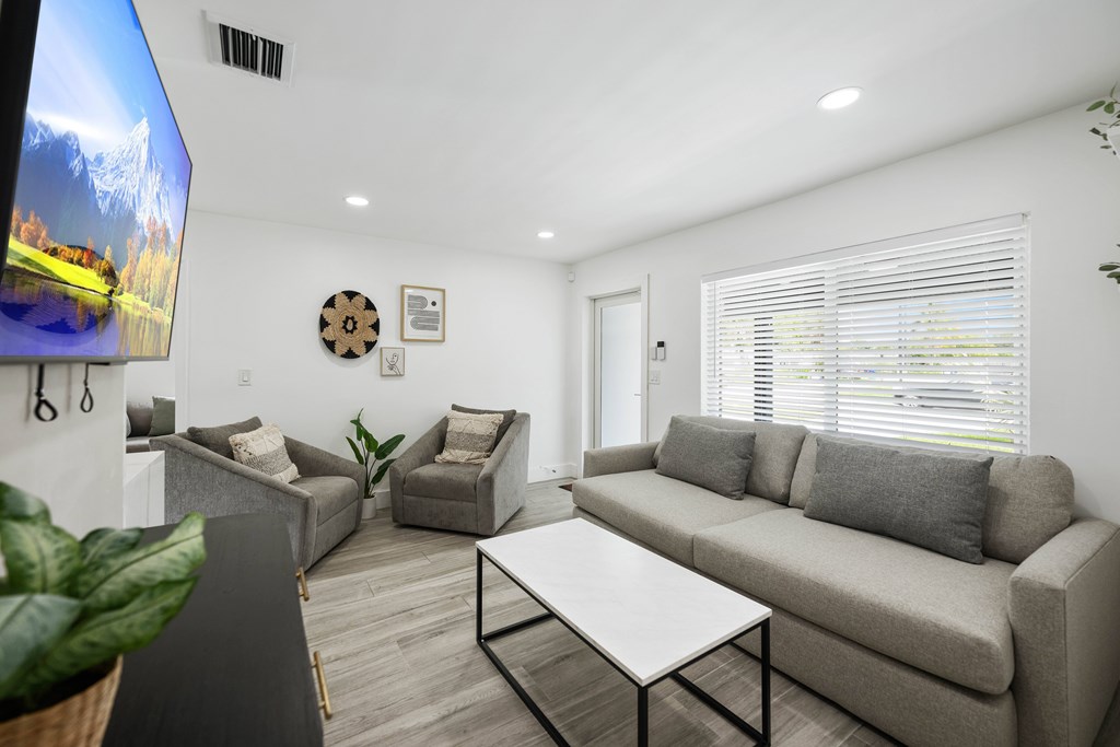 A living room with a grey couch, a white coffee table, and a TV on the wall.