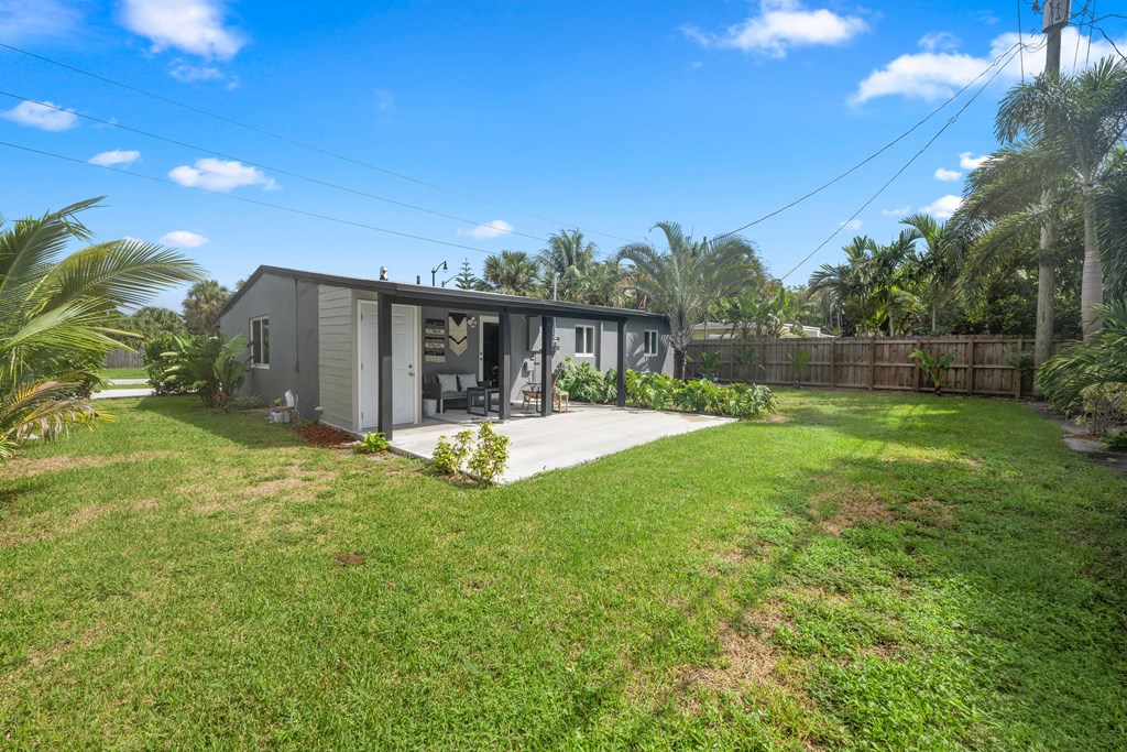 A house with a grey exterior is surrounded by a green lawn and palm trees.