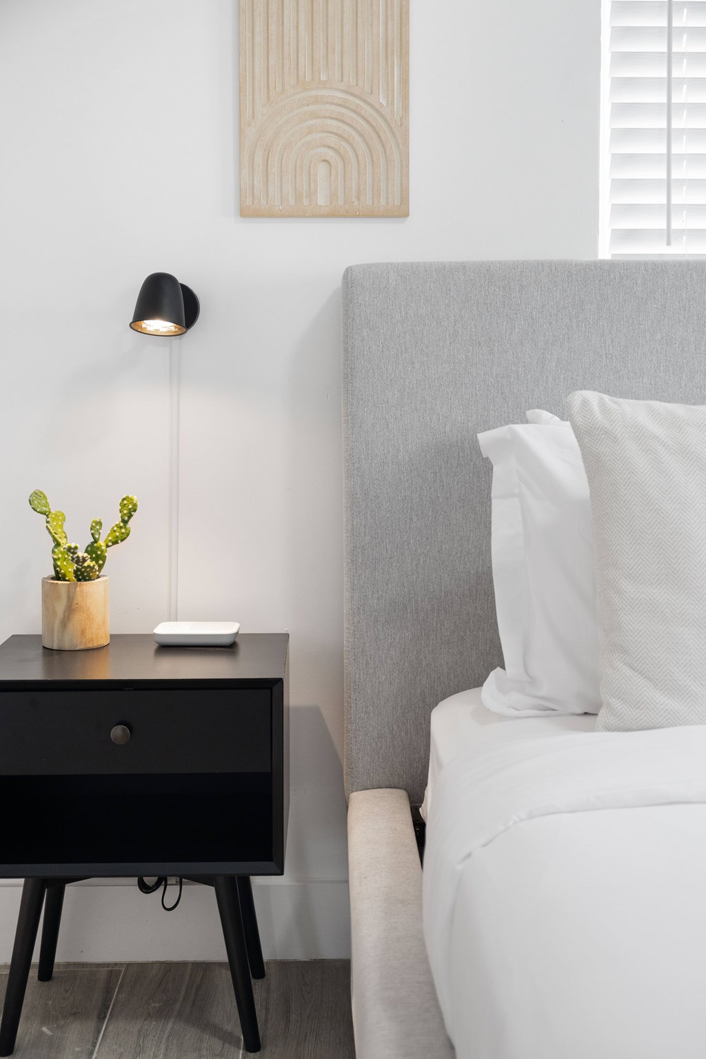 A black drawer with a plant on top sits next to a white bed.