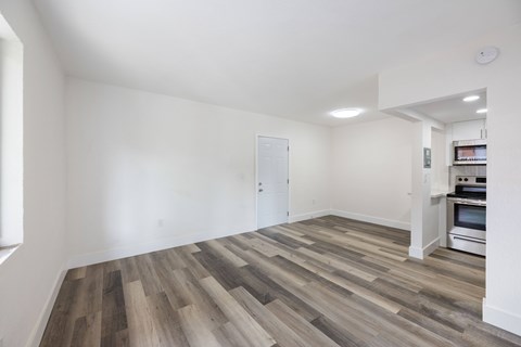 A room with a wood floor and a kitchen in the background.