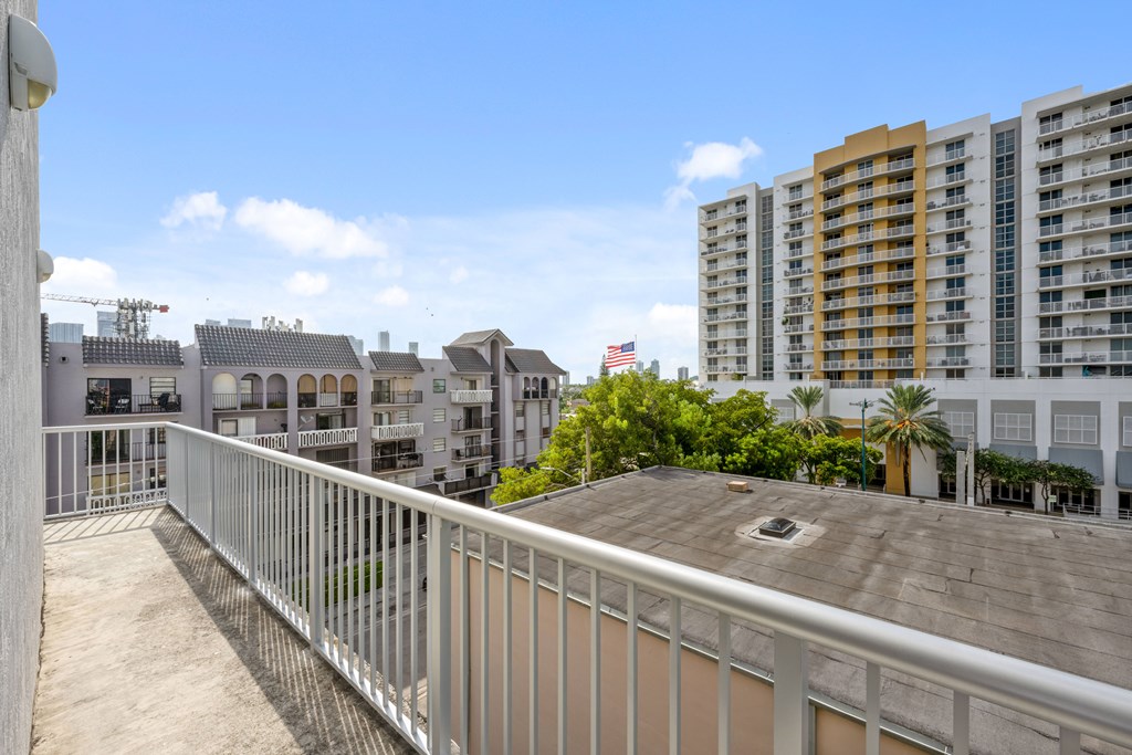 A balcony with a metal railing overlooks a cityscape with buildings and palm trees.