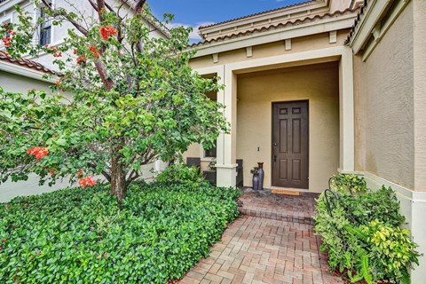 A house with a brown door and a tree with red flowers in front.