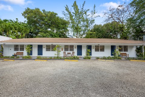 A white building with blue doors and windows is surrounded by trees.