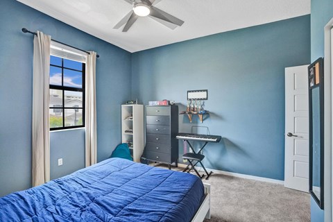 A bedroom with a bed, a window, a fan, and a desk with a chair.