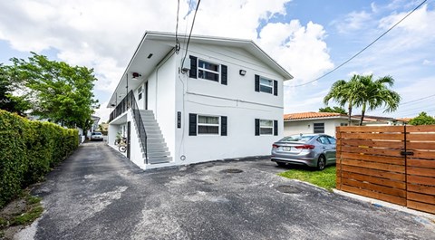 A white two-story house with a grey driveway and a wooden fence.