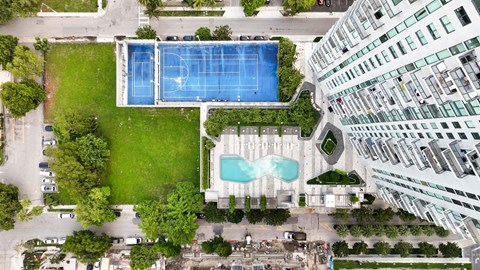 A large swimming pool is surrounded by a grassy area and a tennis court.