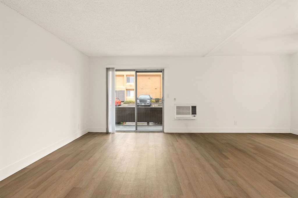 A room with a wooden floor and a white ceiling with a doorway leading to a balcony.