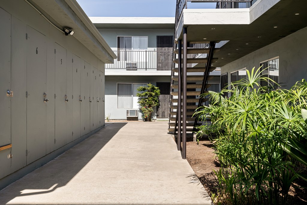 A concrete pathway leads to a building with a balcony and a staircase.