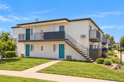 A white and blue two-story apartment building with a balcony on the second floor.