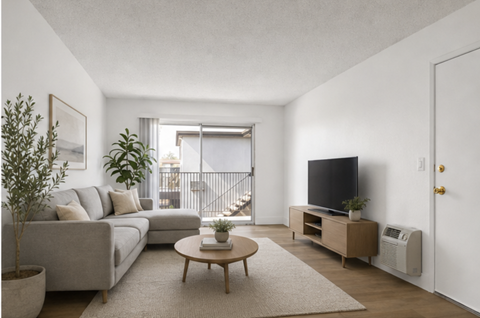 A living room with a grey couch, a coffee table, a flat screen TV, and a potted plant.