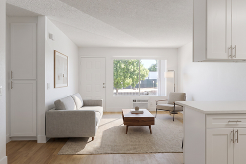 A living room with a grey couch, a coffee table, and a window with a view of trees and buildings outside.