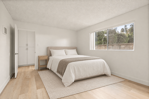 A bedroom with a bed, nightstand, and a window overlooking a fence.